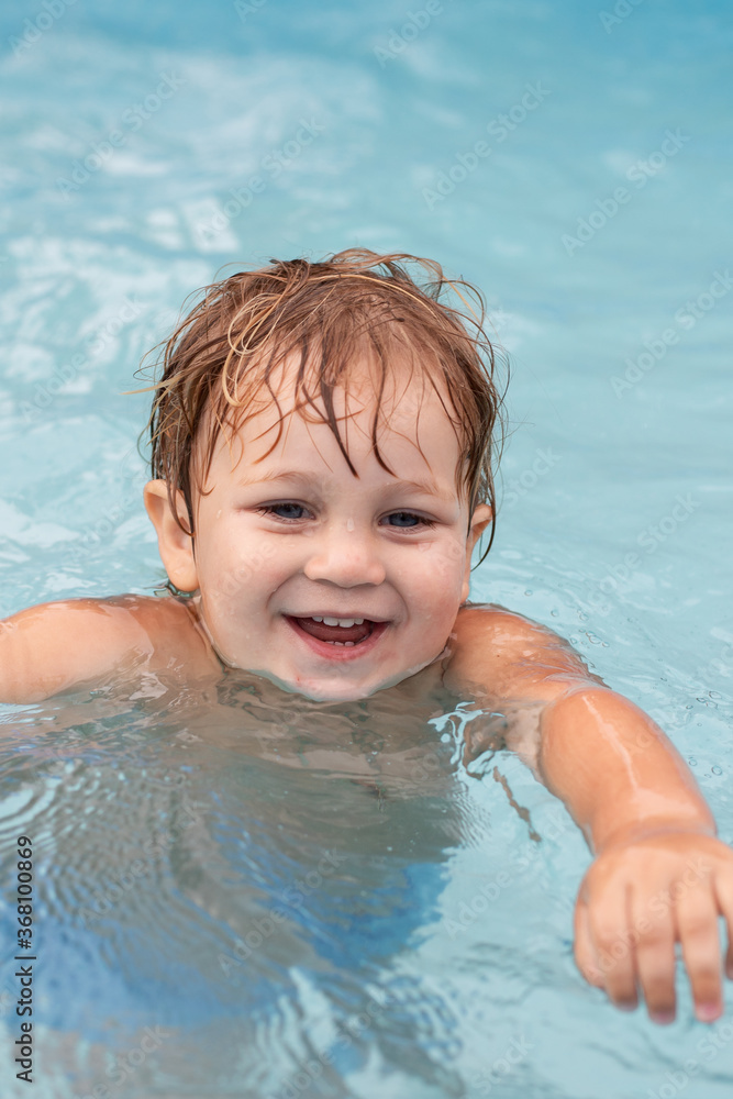 a smiling two-year-old boy swims in a pool a smiling two-year-old boy swims in a pool