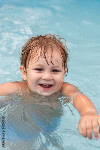 a smiling two-year-old boy swims in a pool 