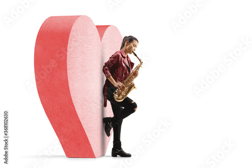 Young woman playing a saxophone and leaning on a red heart photo