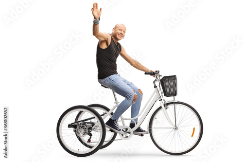 Profile shot of a bald guy riding a tricycle and waving at the camera