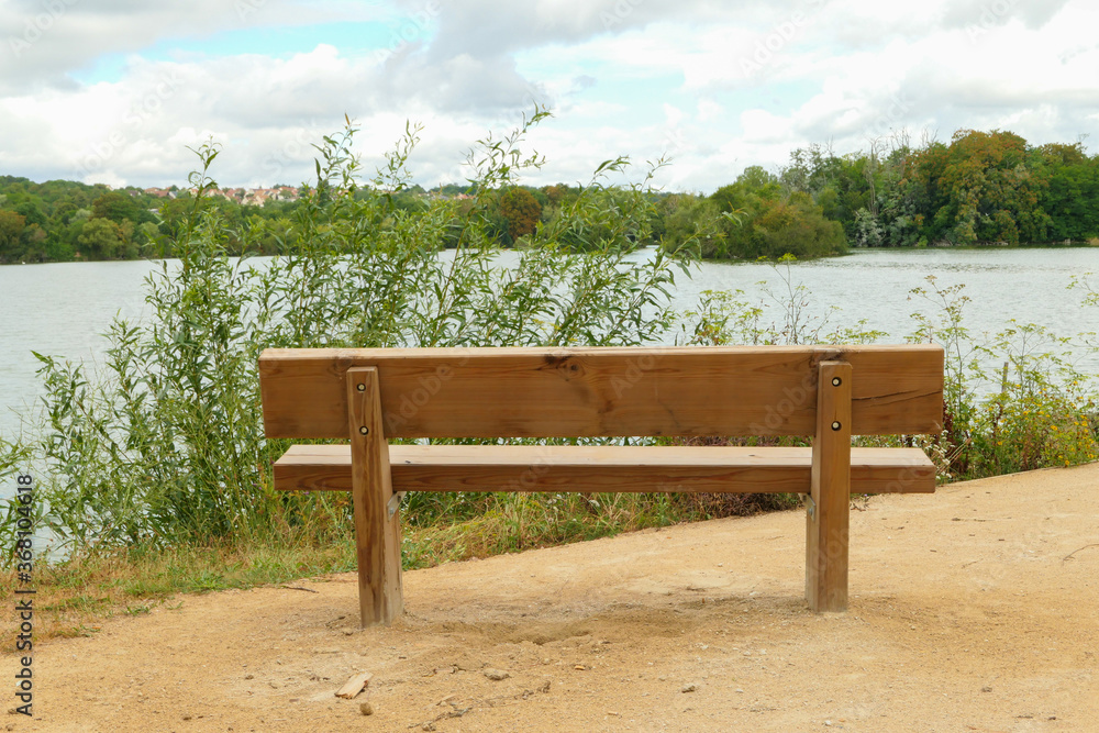 Rural landscape by the water. Isolated bench on the sand, facing a lake with the forest in the background on the horizon.