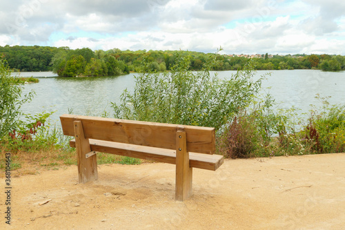 Rural landscape by the water. Isolated bench on the sand, facing a lake with the forest in the background on the horizon.