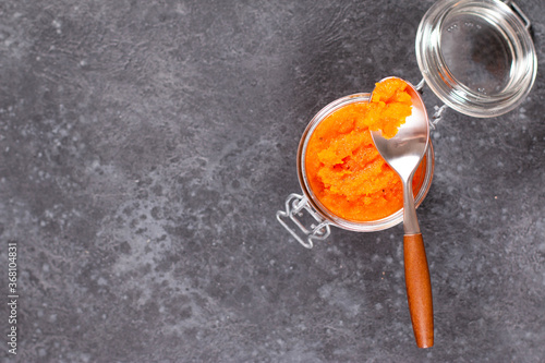 Carrot jam with orange in a glass jar on a dark concrete background. Vegetable jams, copy space, top view