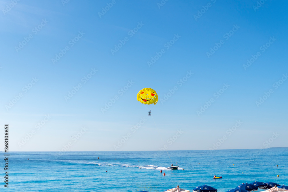 Tourists in bathing suits watch as a boat with a parasailing couple takes off over the Bay of Angels on a sunny summer day on the French Riviera Tourists in bathing suits watch as a boat with a parasailing couple takes off over the Bay of Angels on a sunny summer day on the French Riviera