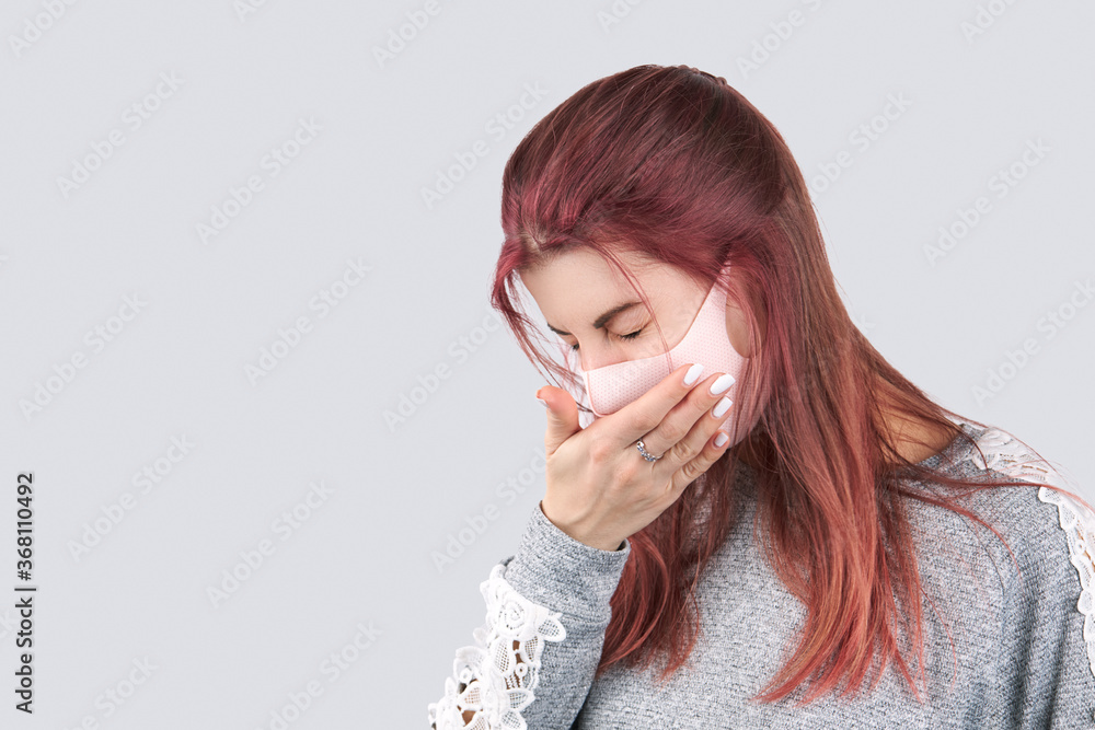 young caucasian woman sneezes or coughs girl wearing face mask and dressed with casual clothes. isolated over gray background with copy space. young caucasian woman sneezes or coughs girl wearing face mask and dressed with casual clothes. isolated over gray background with copy space.