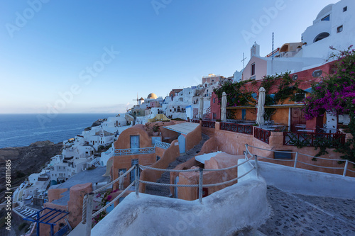 Santorini - Oia, picturesque white houses built at the foot of the caldera, narrow stone walkways lined with white railings. in the foreground sitting under a blooming oleander.