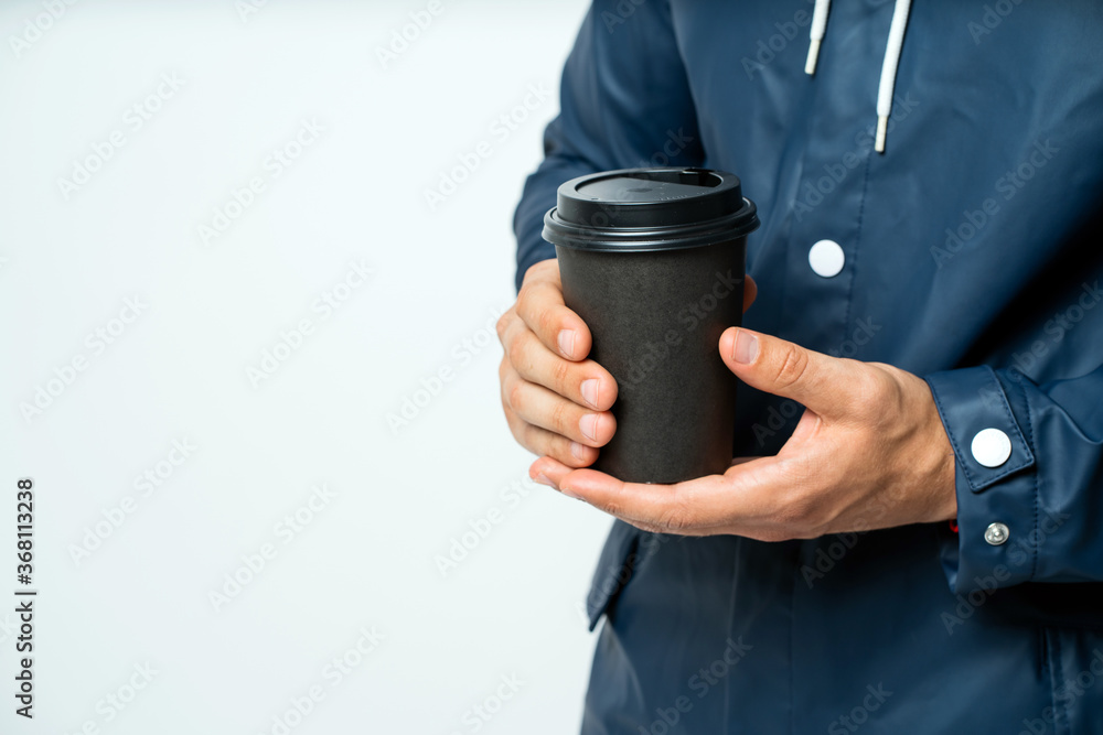 a brown paper Cup with a lid, held by a man in a raincoat.