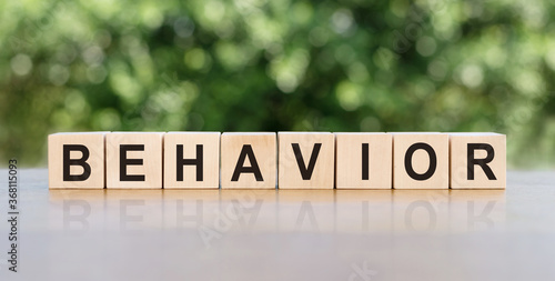 Behavior word written on wooden blocks. The text is written in black letters and is reflected in the mirror surface of the table. © Nastassia