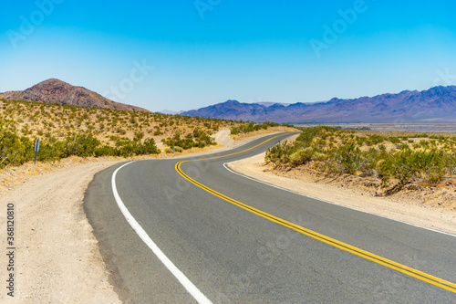 Curved rural road in the Mojave Desert near Barstow, California, with mountains in the background. photo