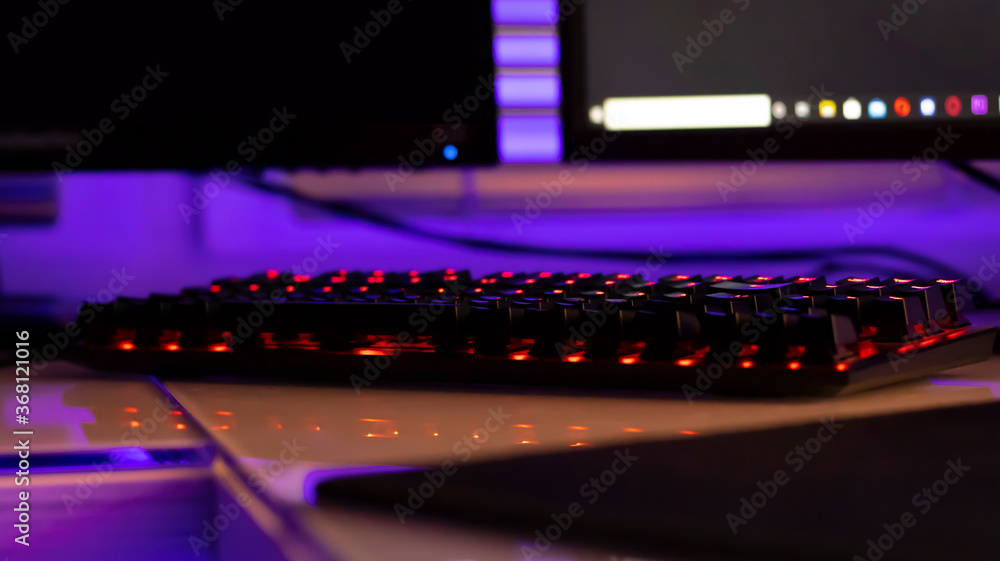 Neon backlit keyboard on white glossy table, close-up. Dark room, neon light, diodes. Gaming devices, neon lights, white glossy table. Lifestyle, game 