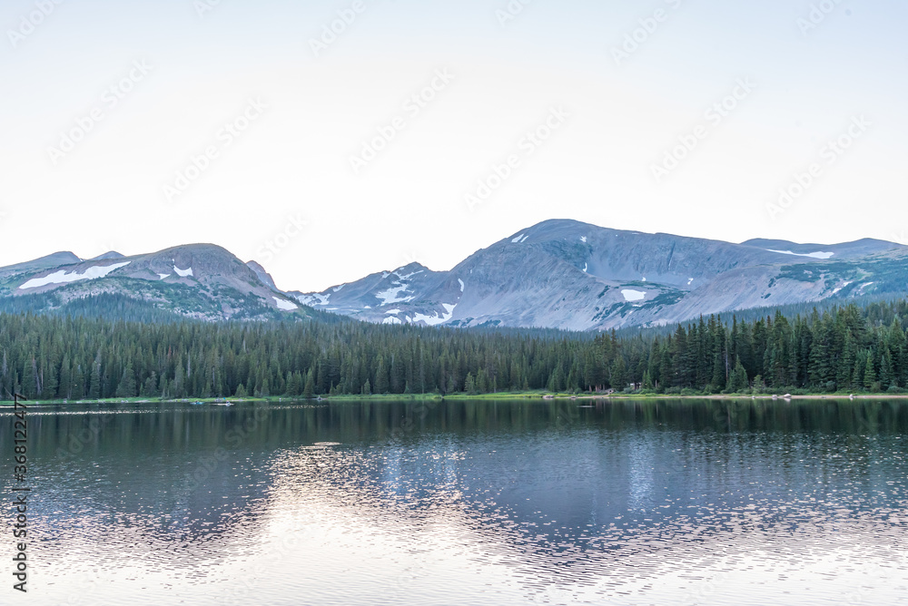 Mountains with snow near lake with evergreen forest trees and hiking trails