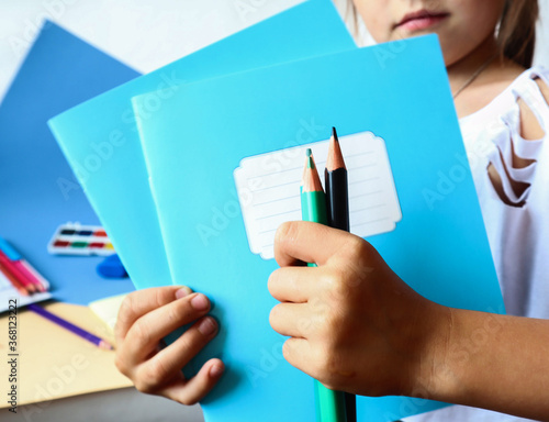  Colored pencils in the hands of a child on the background of school notebooks, side view