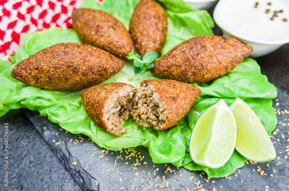 Delicious Lebanese food, kibbeh (kibe) with sauces and lemon on black