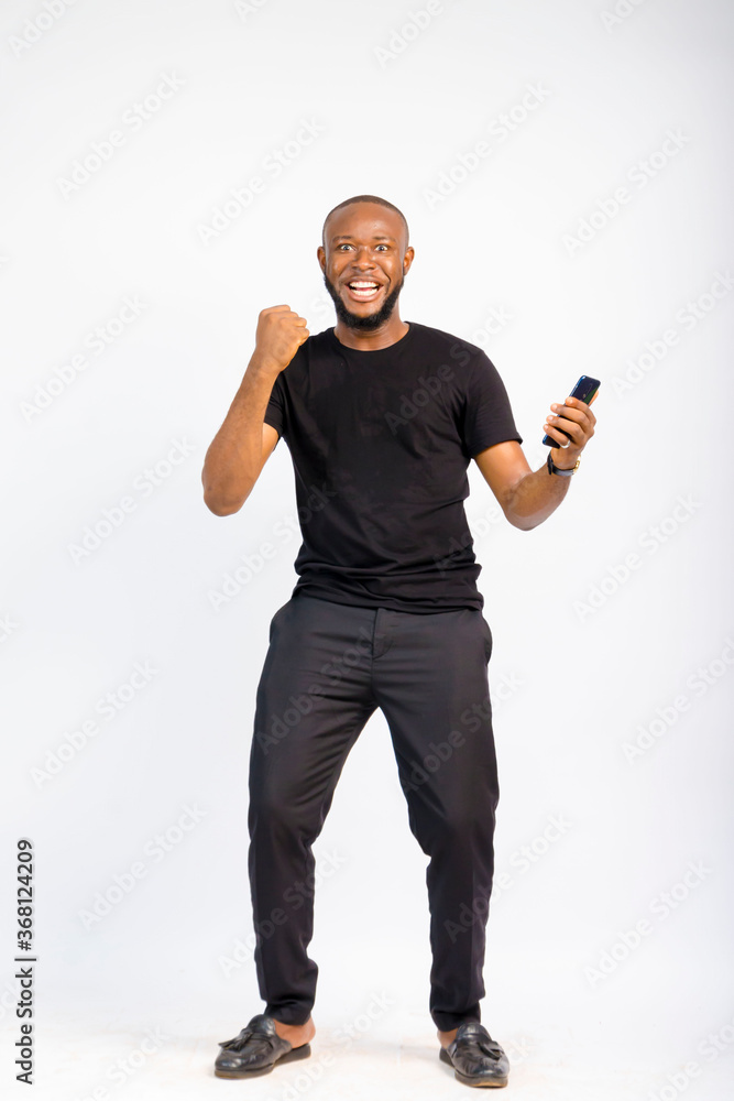 young black handsome man standing jubilating over something he saw on his smartphone young black handsome man standing jubilating over something he saw on his smartphone