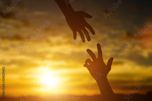 Silhouette of giving a help hand, hope and support each other over sunset background. Concept of helping hands and develop a friendship.