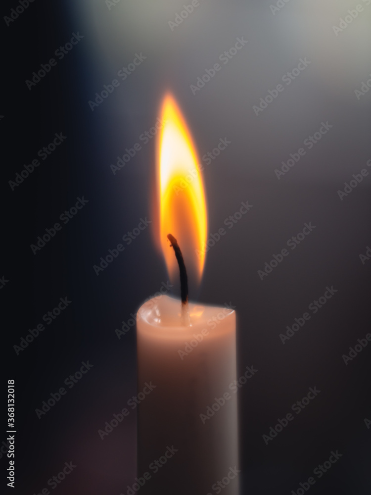 Close-up of a shining and glowing candle light with a warm flame and a blurry dark background Close-up of a shining and glowing candle light with a warm flame and a blurry dark background
