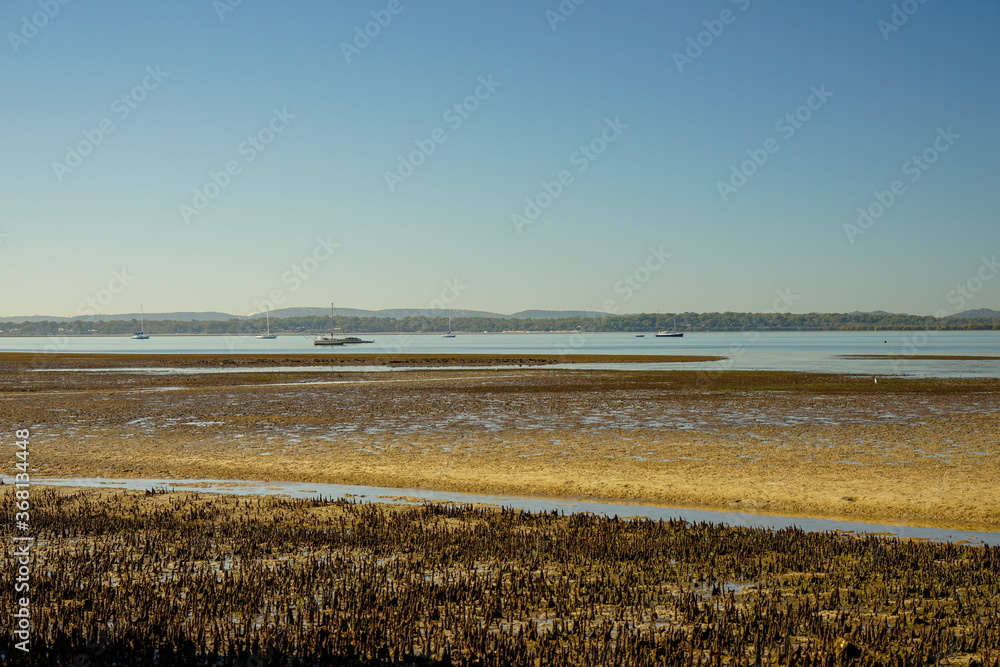 View over low tide sand flats to boats moored in the bay, and islands on the horizon,. Redland Bay, Queensland, Australia.