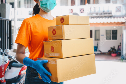 Delivery service courier holding boxes mail for sending to customer while wearing mask and glove for protect herself in covid-19 pandemic outbreak.