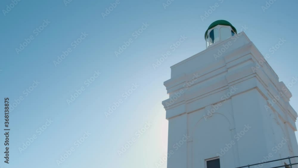 Upward shot of the top of a lighthouse coming into view against a blue sky Upward shot of the top of a lighthouse coming into view against a blue sky