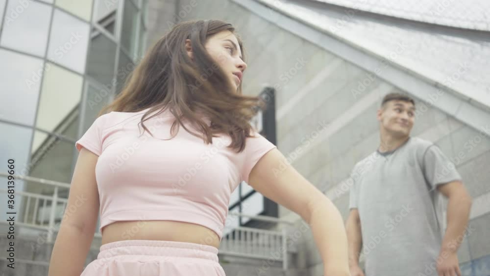 Portrait of gorgeous Caucasian woman and handsome man performing dance movements as standing on urban stairs outdoors. Happy Caucasian man and woman dancing in city and smiling at camera. Portrait of gorgeous Caucasian woman and handsome man performing dance movements as standing on urban stairs outdoors. Happy Caucasian man and woman dancing in city and smiling at camera.
