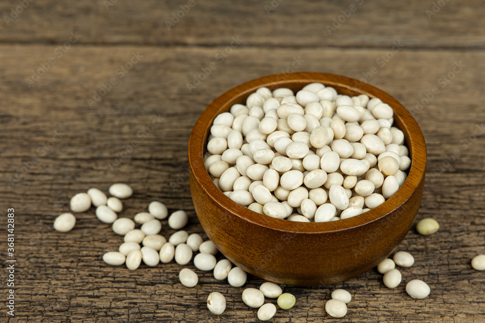 Raw white beans seed in wooden bowl on wooden table background. Raw white beans seed in wooden bowl on wooden table background.