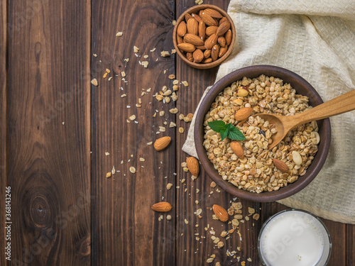 Milk, almonds and granola in a clay bowl on a wooden table.