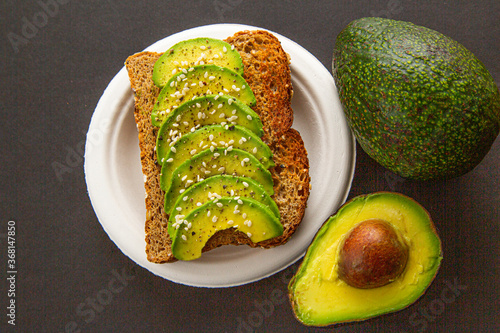 avocado sandwich on dark rye bread made with fresh sliced avocados and sesame seeds. on plate