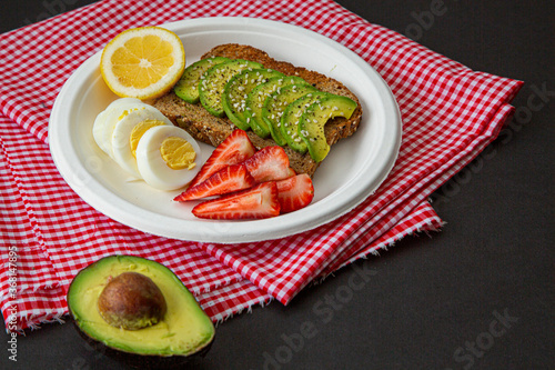 delicious and healthy breakfast of avocado sandwich with egg, strawberry and lemon on black background