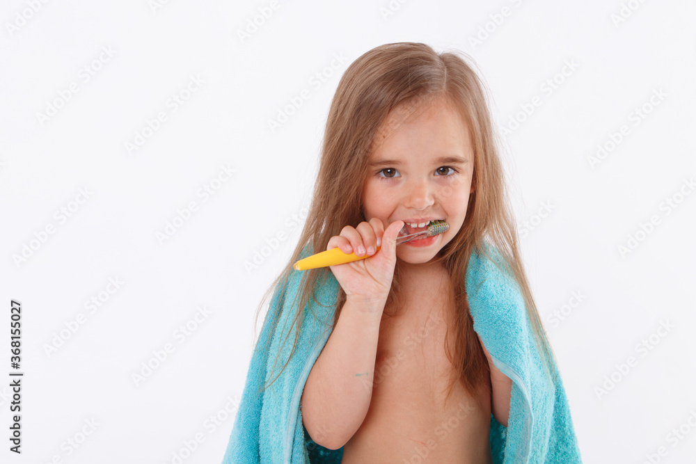 a little girl brushes her teeth on a white background. portrait of a child with a yellow toothbrush. blue towel around her neck. morning hygiene procedures a little girl brushes her teeth on a white background. portrait of a child with a yellow toothbrush. blue towel around her neck. morning hygiene procedures
