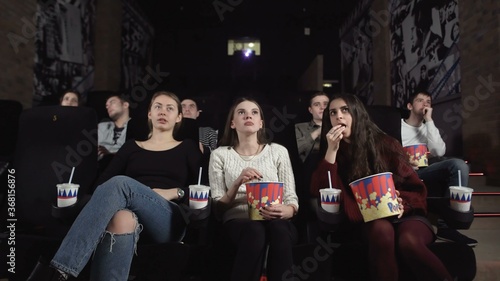 Three pretty female friends are watching a scary movie.Middle woman reacts with shock.