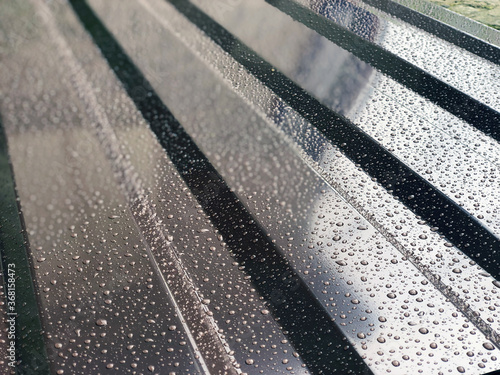 Wavy sheet of a metal profile of brown color in drops of rain with a glare close-up