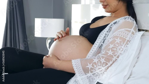 happy pregnant woman resting and hands pat the pregnant belly on the bed