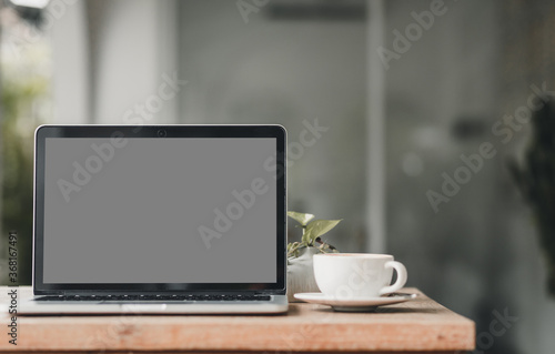 Mockup of laptop computer with empty screen with coffee cup on table of the coffee shop background,gray screen