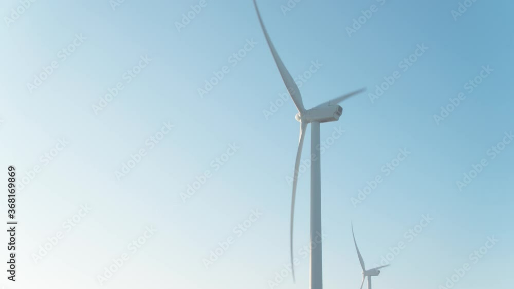 Windmill turbines rotating against blue sky. Zoom in, low angle Windmill turbines rotating against blue sky. Zoom in, low angle