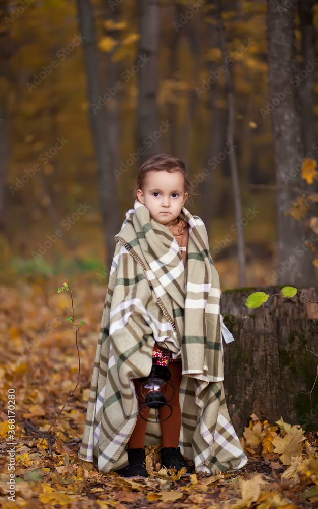 Little girl on a brown coat and warm plaid holds lamp outdoors. Autumn time. Happy child playing at fall nature background. Autumn mood. Kids autumn fashion. Happy childhood. Little girl on a brown coat and warm plaid holds lamp outdoors. Autumn time. Happy child playing at fall nature background. Autumn mood. Kids autumn fashion. Happy childhood.