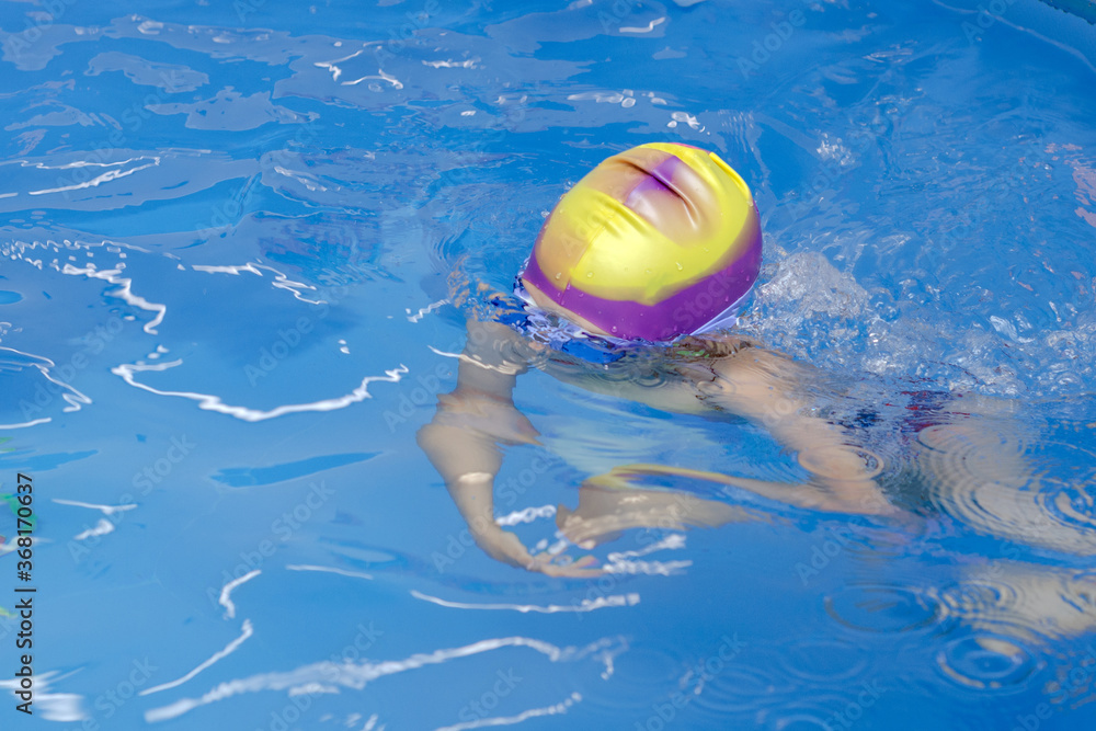 a child with a rubber cap on his head swims in the pool