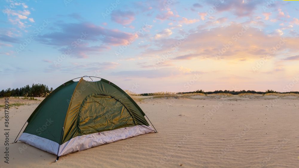 green touristic tent in a sandy desert at the sunset, evening travel scene