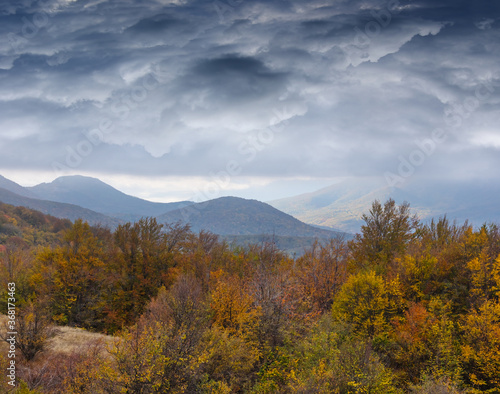 mountain valley with autumn forest under a dense dramatic clouds