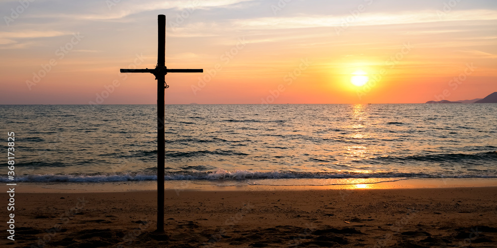Dark cross at beach as the sun sets over the sea. Cross symbol over the setting sun. Sunset at the beach Dark cross at beach as the sun sets over the sea. Cross symbol over the setting sun. Sunset at the beach