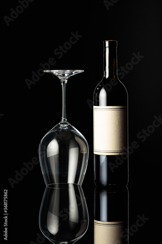 Bottle of red wine and an inverted wine glass on a black background.
