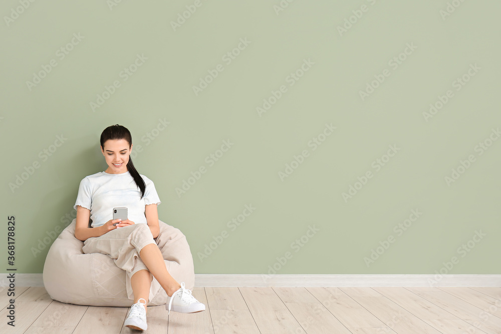 Ταπετσαρία Young woman with mobile phone relaxing on beanbag near color wall