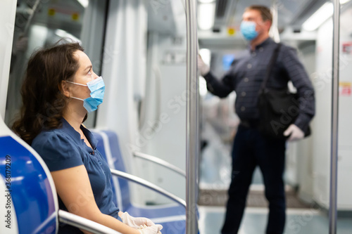 Young brunette in medical face mask and protective gloves riding in modern subway car. Concept of forced city trip in context of coronavirus pandemic..