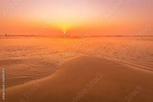 A colorful sunset or sunrise on the seaside with a sandy beach with impurities of volcanic ash. Mandrem, Goa, India. photo