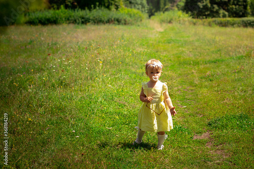 cute little baby girl in yellow dress looking at the camera at the garden