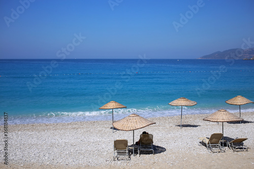 Pebbled sandy beach with wooden umbrellas  Mediterranean coast near the resort town of Fethiye in Turkey.