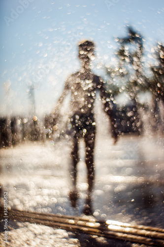 Fototapeta Naklejka Na Ścianę i Meble -  The silhouette of a boy is seen behind the drops of water in the fountain