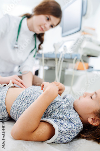 Attentive doctor looking at girl while pressing fingers against her stomach