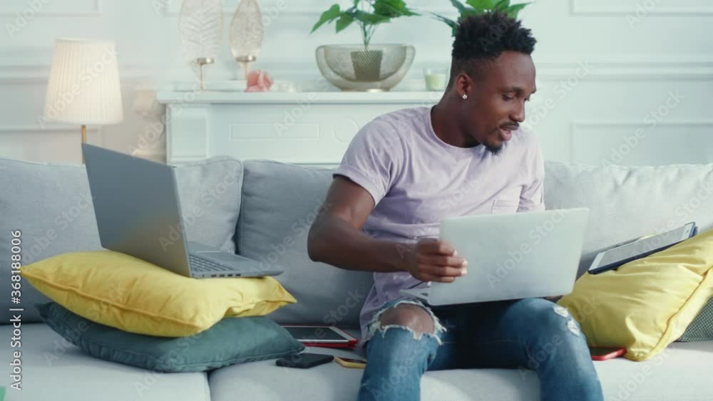 Busy afro-american young businessman employee working from home using several laptops and tablet for remote communication video call conference. Multi-tasking.