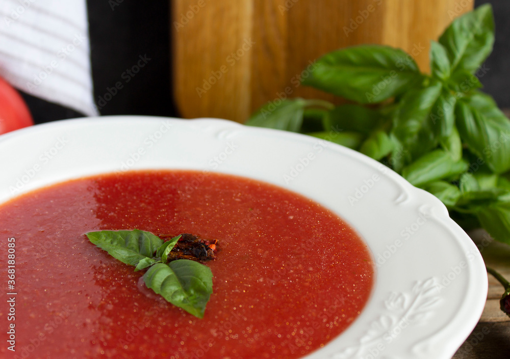 Cold gazpacho soup in a white plate with green basil leaves, close-up Cold gazpacho soup in a white plate with green basil leaves, close-up