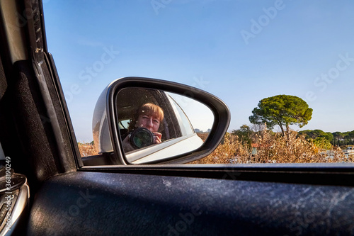 Car Mirror and reflection of traveller photographer and sky in it. photo